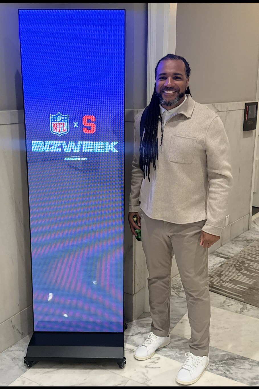 Usama Young smiling in a hotel hallway beside an event display