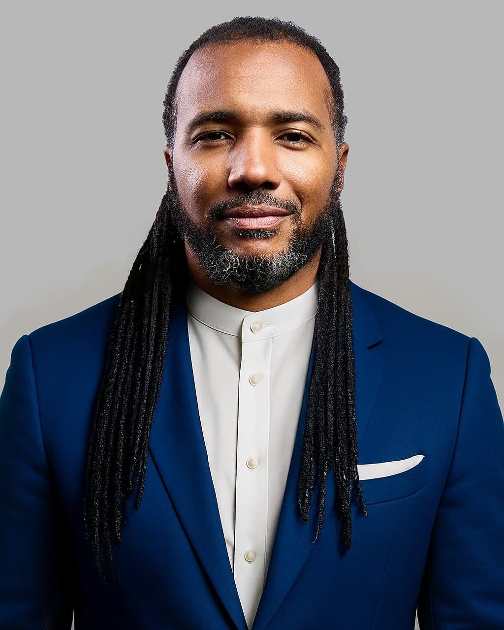 Usama Young in a navy suit and white collar, looking at the camera